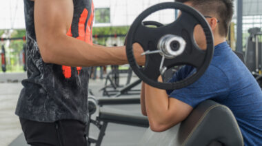 A person performs a forced rep with the help of a spotter in the gym.