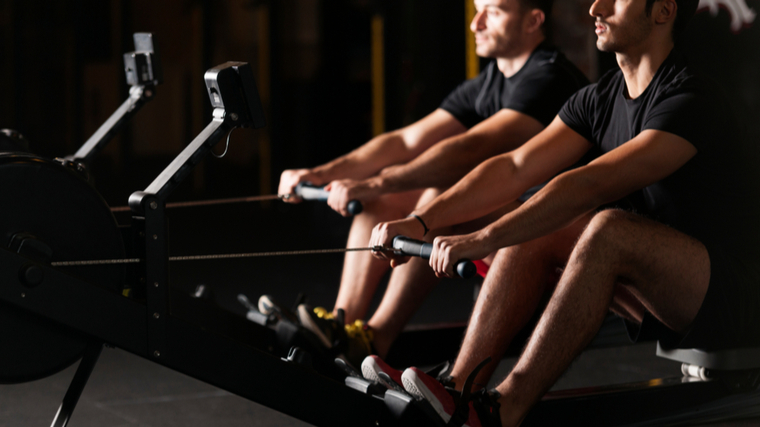 Two people prepare to row in the gym.