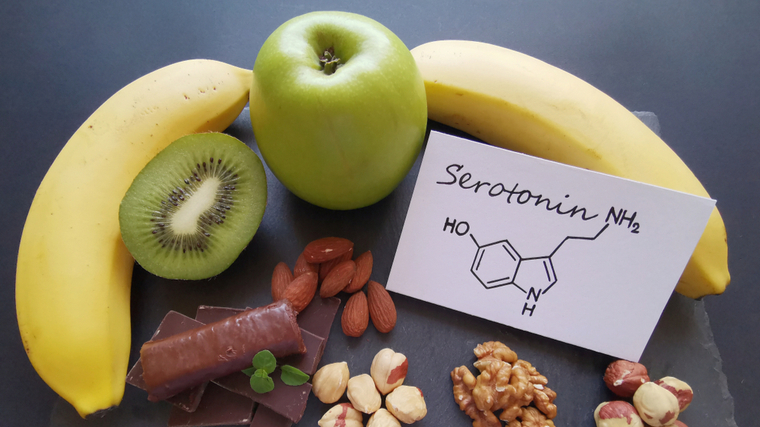 Foods like bananas, kiwis, and mixed nuts sit on a table with an index card that says "serotonin."