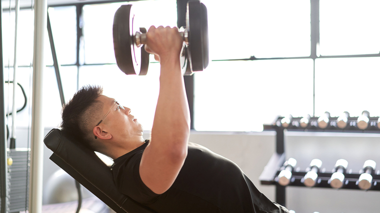 A person performs dumbbell flyes at the gym.