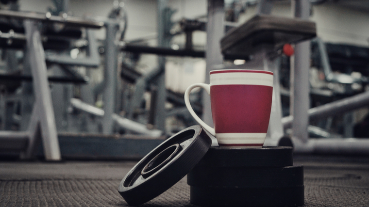 A mug of coffee sits on top of some small weight plates in the gym.