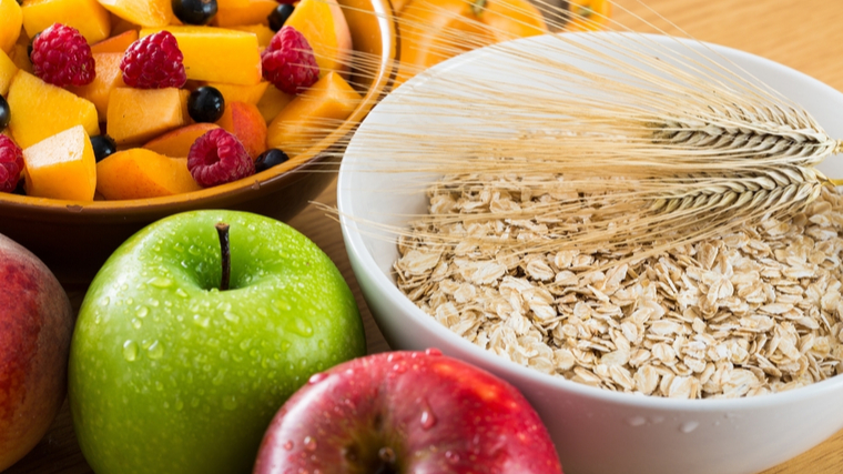 A bowl of fruit sits beside apples and a bowl of oats.