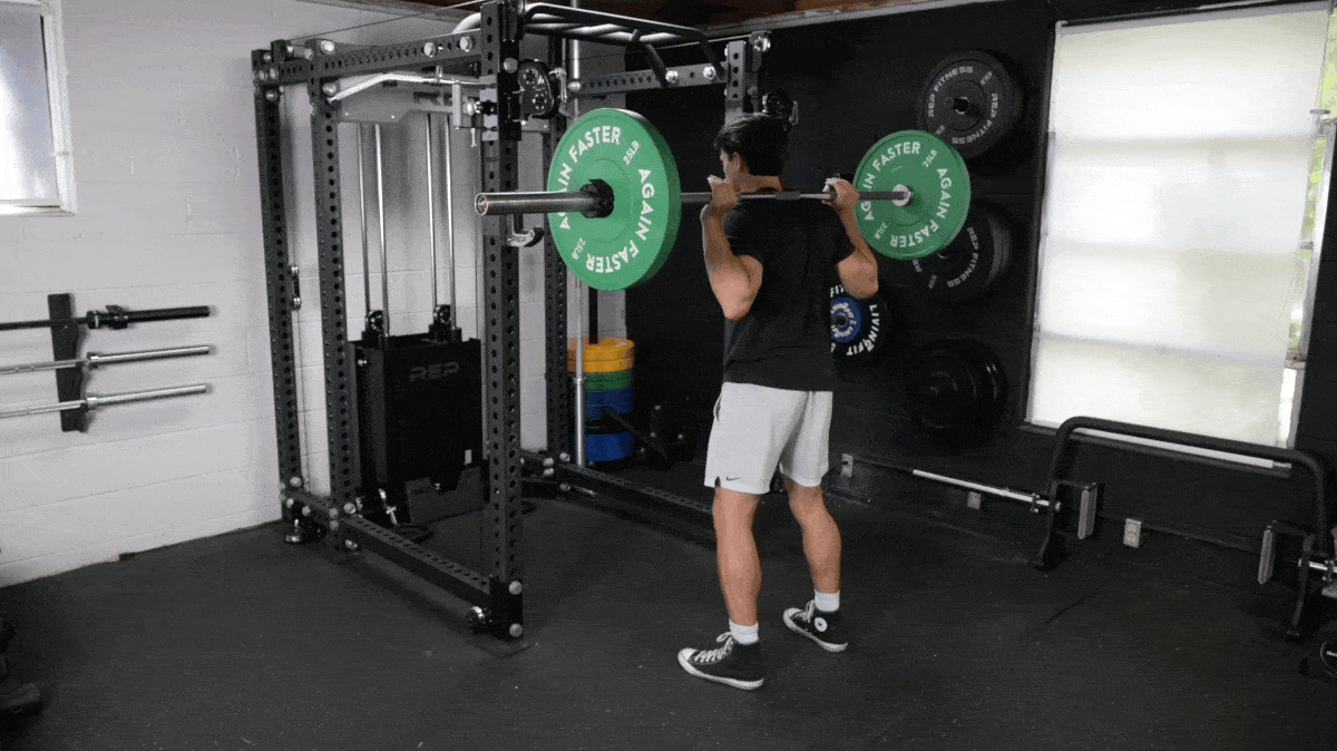 A person doing back squats in the Barbend gym.