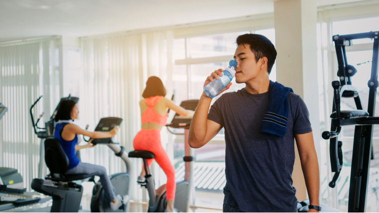 A person sips from a water bottle at the gym.
