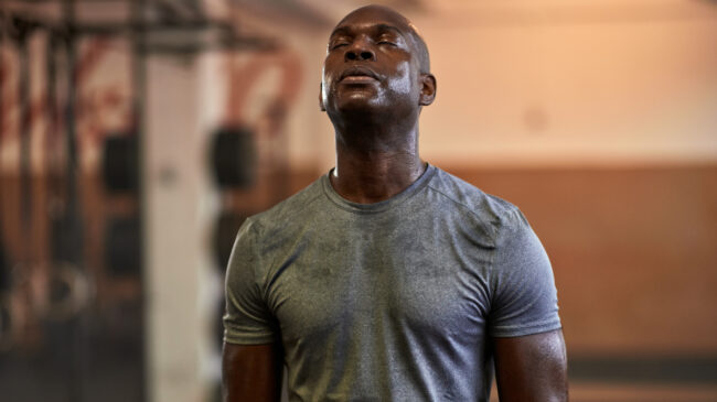 A person closes their eyes and lifts their head while sweating from a workout.