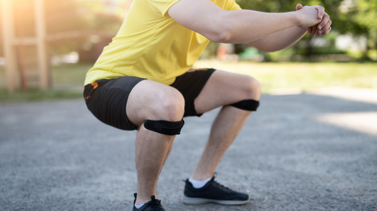 A person squats while wearing two knee straps.