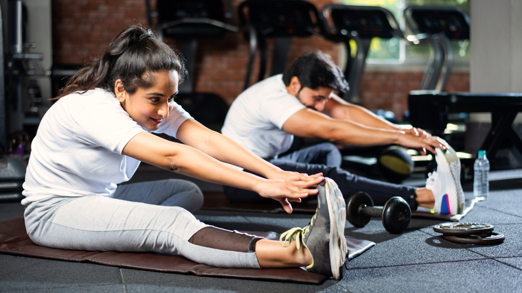 Two people perform hamstring strecthes on yoga mats.