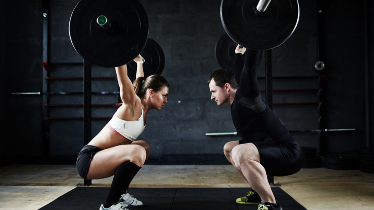 Two people perform barbell snatches across from each other.