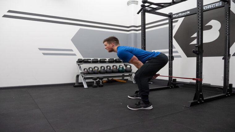 A person in a blue t-shirt starting to hinge up to standing while performing a cable pull-through.