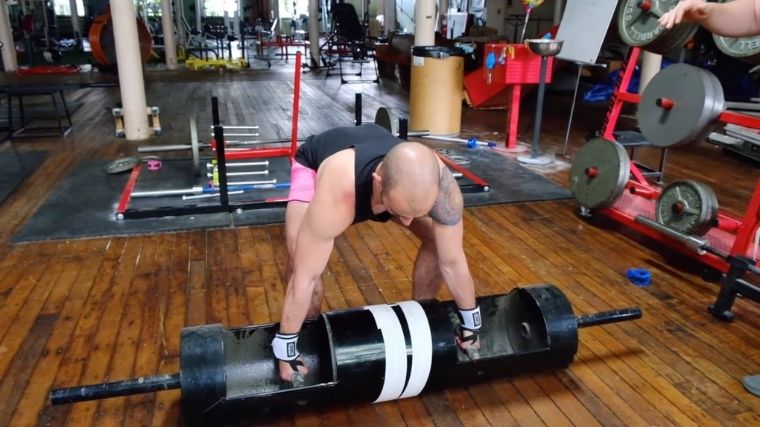A person wearing pink shorts prepares to deadlift a log implement.