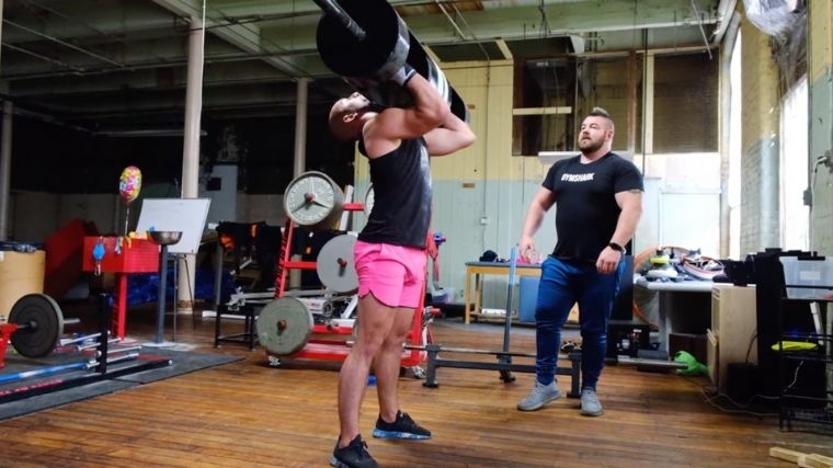 A person wearing pink shorts supporting a strongman log implement in the front rack position