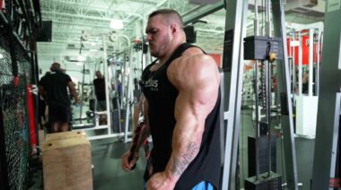 Nick Walker performing triceps pushdowns with a rope attachment, facing away from the cable stack