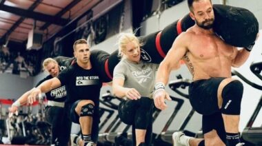 Team CrossFit Mayhem performing a set of walking lunges with a large sandbag resting on all four team member's shoulders