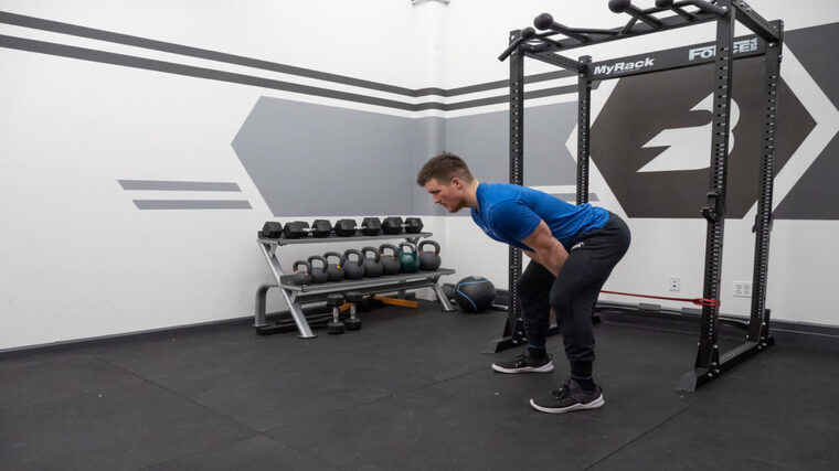 A person wearing a blue t-shirt hinges back while performing a cable pull-through with a red resistance band.