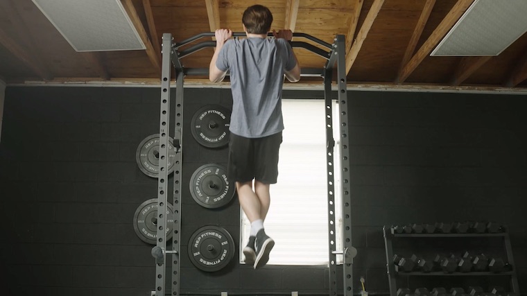 Our tester tests the pull-up bar of the REP PR-1100 at the BarBend garage gym.