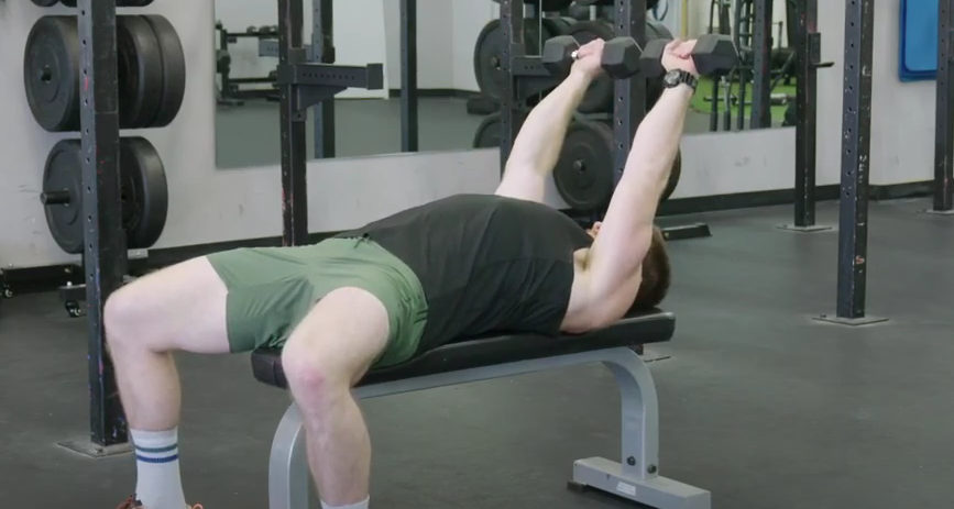 A person sets up to perform a dumbbell skull crusher on a flat bench.
