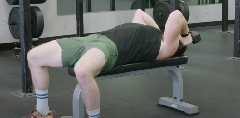 A person performs a dumbbell skull crusher in the gym.