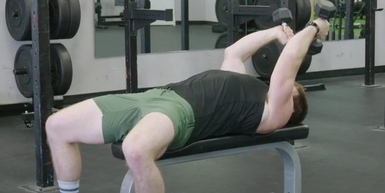 A person performs a dumbbell skull crusher in the gym.