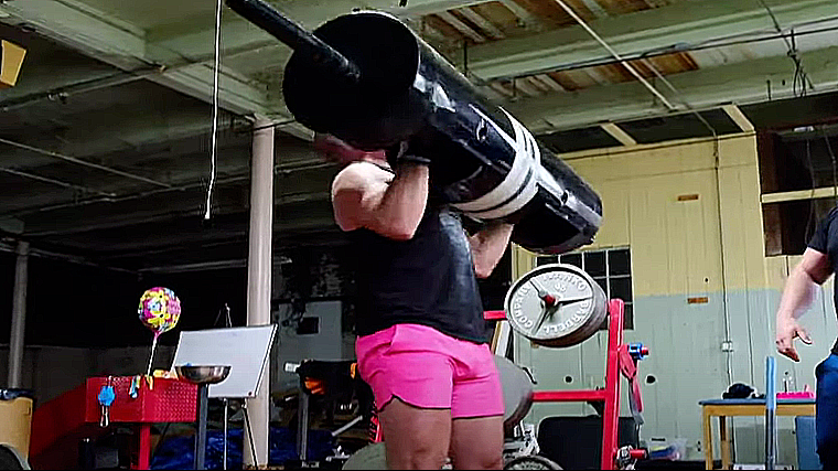 A person wearing pink shorts lowers a log bar to their chest.
