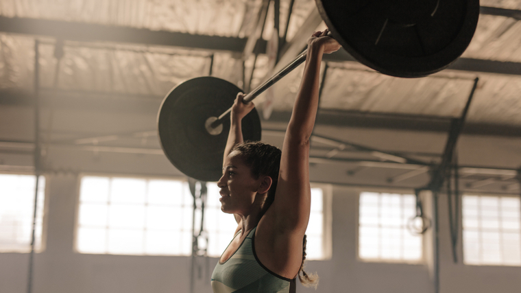 A person smiles slightly with the loaded barbell locked out overhead.