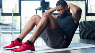 A person wearing a black shirt and red sneakers performs a sit-up.