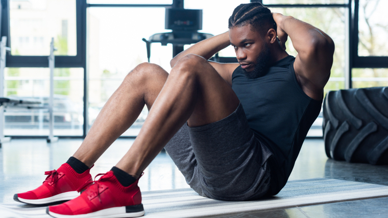 A person wears a black shirt and red sneakers while performing a sit-up.