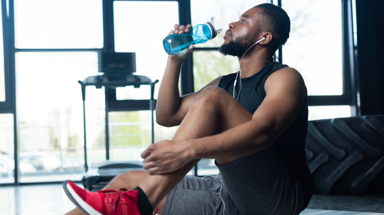 A person sits in the gym and drinks water.