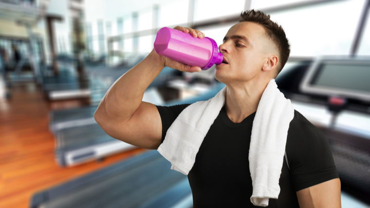 A person drinks water next to a treadmill.