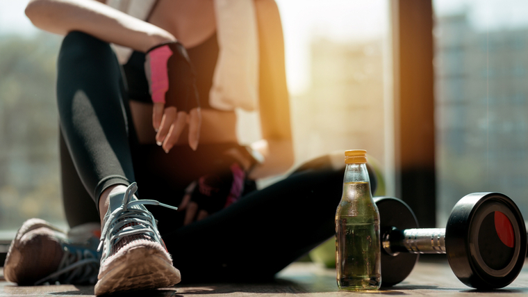 A close-up image of a person sitting on the gym floor in front of a water bottle and a dumbbell.