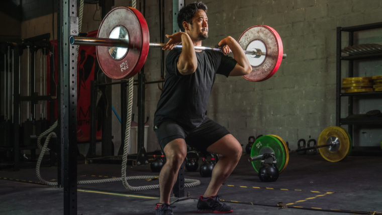 A person wears a black t-shirt while front squatting a loaded barbell.