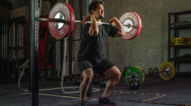 A person wears a black t-shirt while front squatting a loaded barbell.