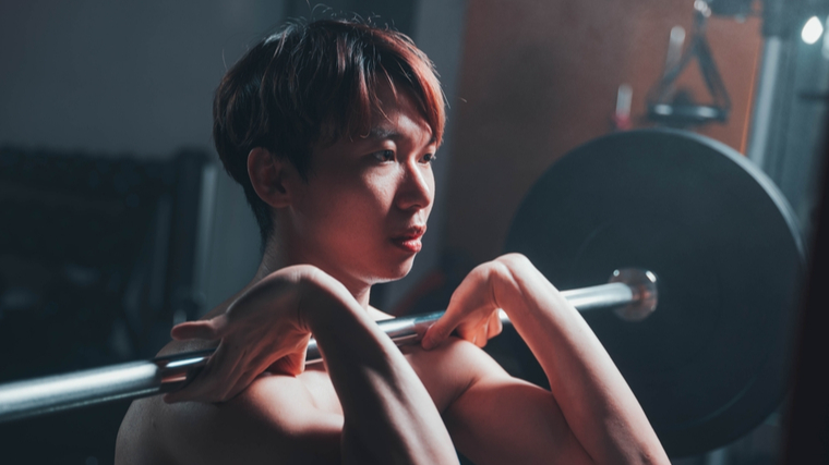 A close up shows a person holding a barbell in the front rack position.