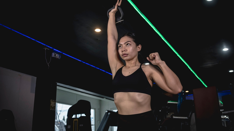 A person holds one kettlebell overhead.