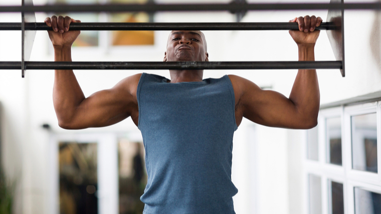 A person wears a blue sleeveless shirt while performing a pull-up.