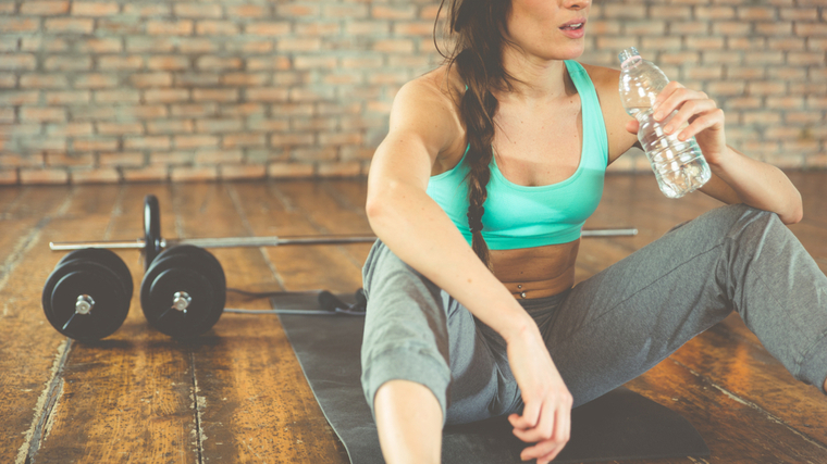 A person sits in front of a barbell and drinks water.