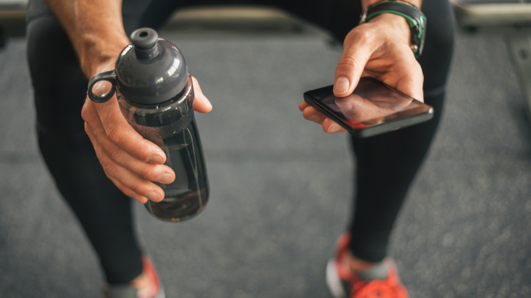 A close-up image shows a person's hands as they sit down holding a water bottle and their smartphone.