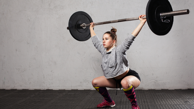 A person with their hair up in a bun performs a barbell snatch.