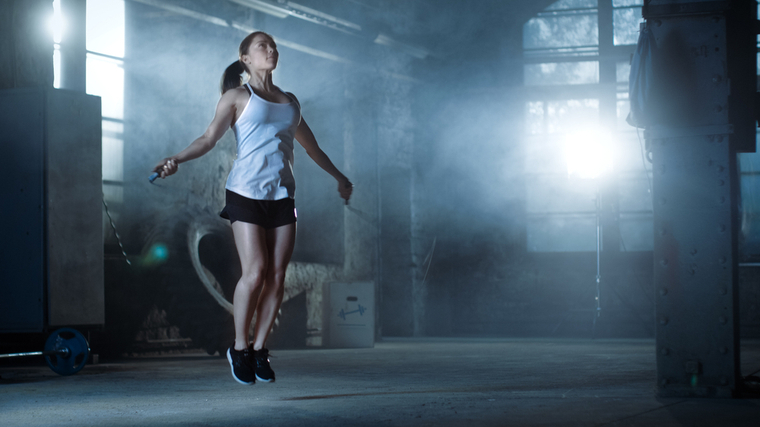 A person wearing a white tank top jumps rope in an empty gym.