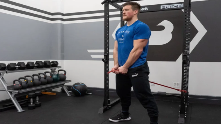 A person wearing a blue t-shirt performs a cable pull-through with a red resistance band.