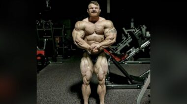 212 Bodybuilder Flex Lewis hitting a most muscular pose in posing trunks, standing in a dark gym