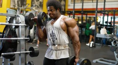 Boybuilder Breon Ansley curling a dumbbell wearing a grey tank top