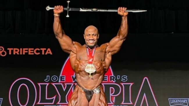 Muscular bodybuilder holding a sword over his head on stage