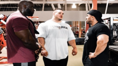 Pro bodybuilders Samson Dauda, Kamal Elgargni, and Nick Walker talk in a gym.