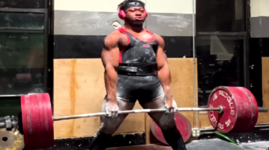 Bobb Matthews deadlifts 845.5 pounds in training while wearing red headphones and a black lifting belt.