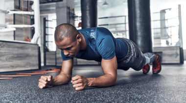 A person wears a blue t-shirt while performing a plank.