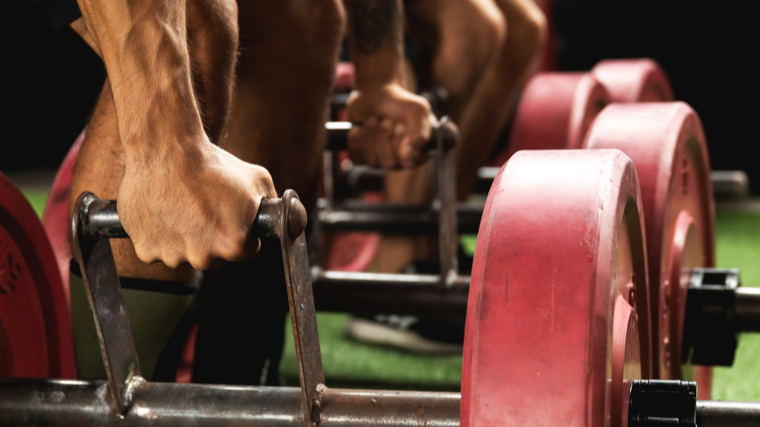 A close up image shows two people's hands getting ready to perform loaded farmer's carries.