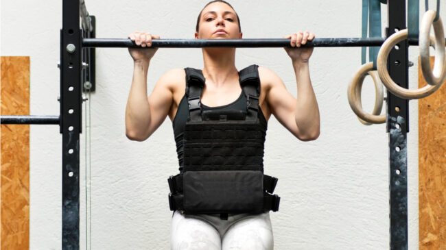 A person wears a weighted vest and peforms a pull-up.