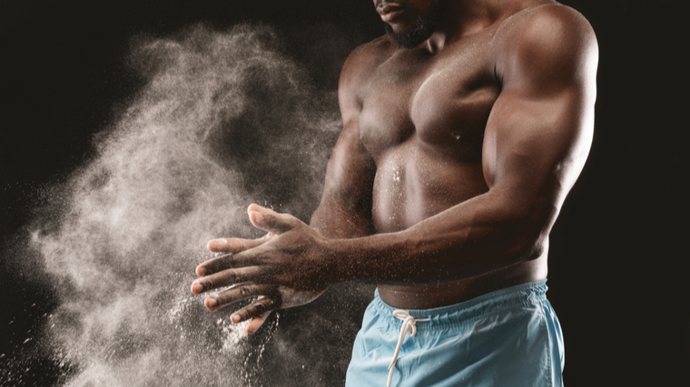 A shirtless person claps chalk in their hands.