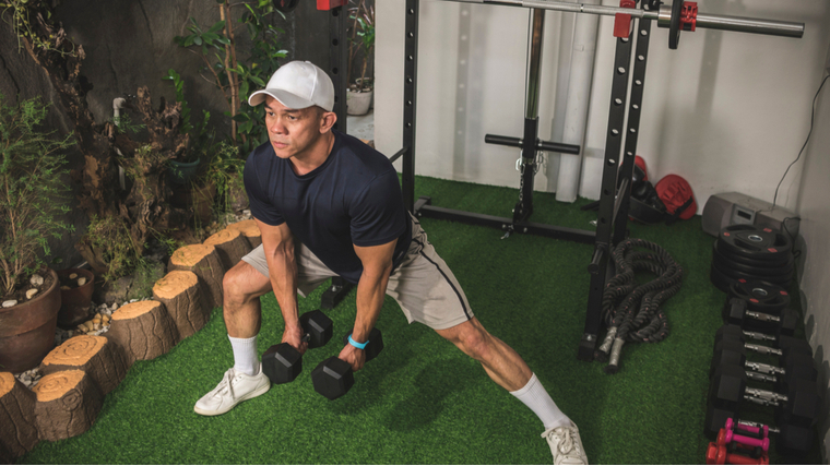 A person wears a white baseball cap while performing lateral lunges with dumbbells.