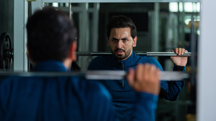 A person wearing a blue long-sleeved shirt looks in the mirror while preparing to squat.